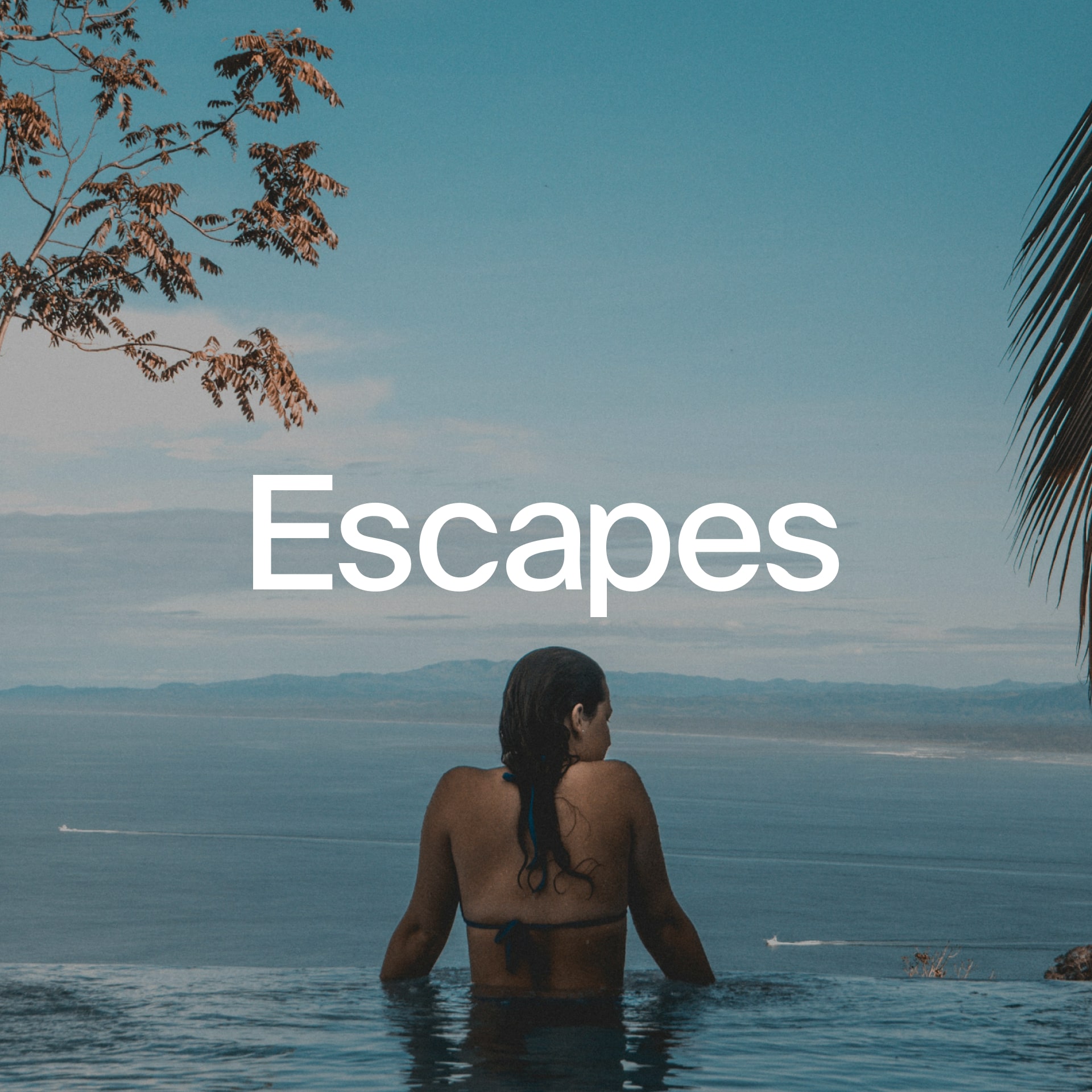 Woman in an infinity pool overlooking the ocean and distant coastline.