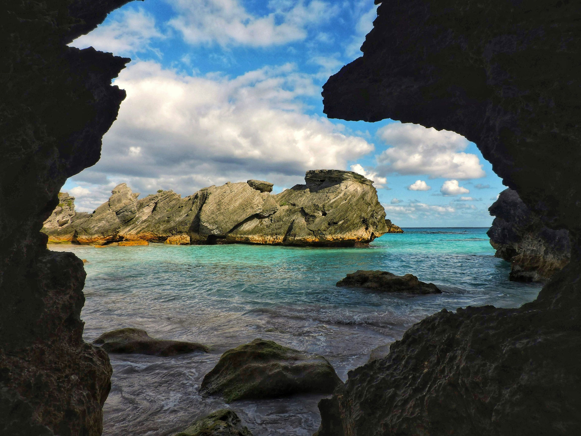 View of rugged coastal rock formations and turquoise waters framed by a natural cave opening in Bermuda