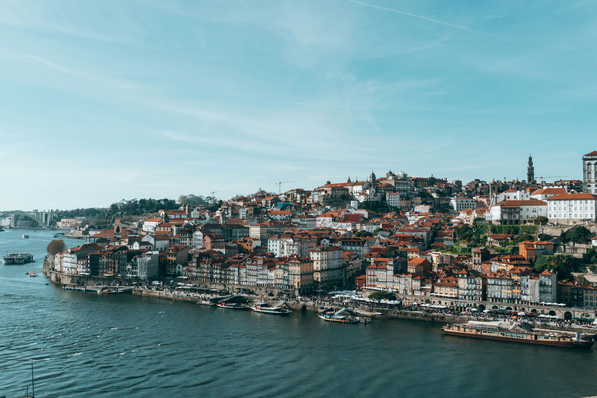 Panoramic view of the Ribeira district in Porto, Portugal, showcasing colorful historic buildings with red-tiled roofs along the Douro River.